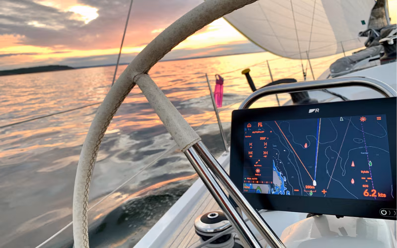Boat-cockpit-steering-wheel-and-chartplotter-displaying-navigation-data-at-sunset