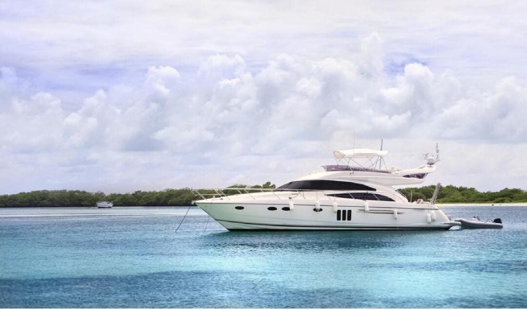 White luxury yacht anchored in clear blue tropical water under a cloudy sky